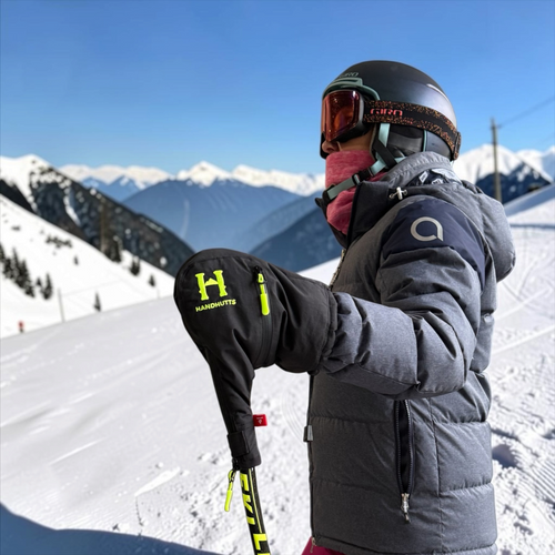 Skier wearing Handhutts LLC insulated black pole hand covers with neon green logo on a snowy mountain slope